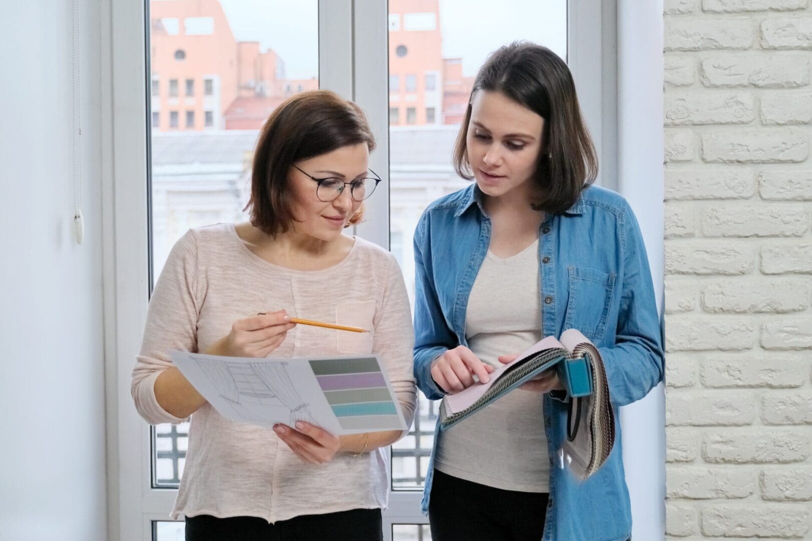 Two women choosing fabrics for curtains. Females textile designer, decorator and client watch palettes with fabrics, choose model and fabric