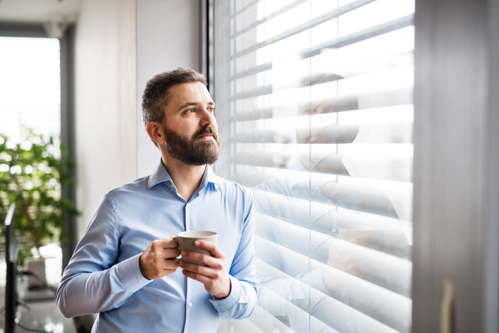 A man standing by the window, holding a cup of coffee. Smart home control system.