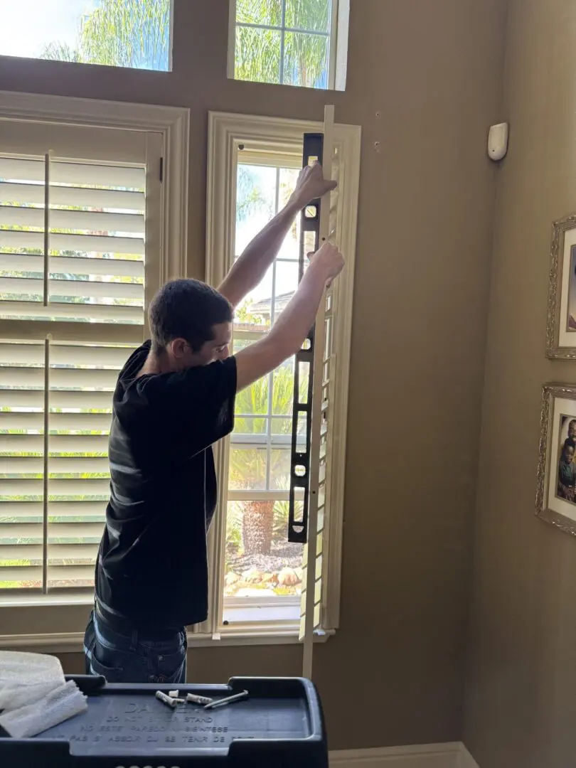 Man leveling window blinds with a tool.