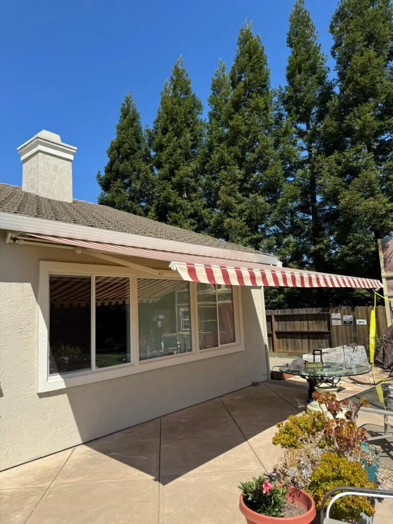 House patio with striped awning and trees.